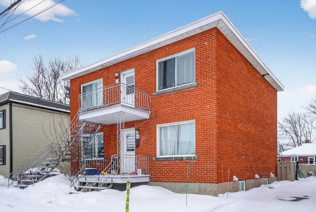 Le duplex de brique rouge et son escalier extérieur, vu de trois quarts en hiver